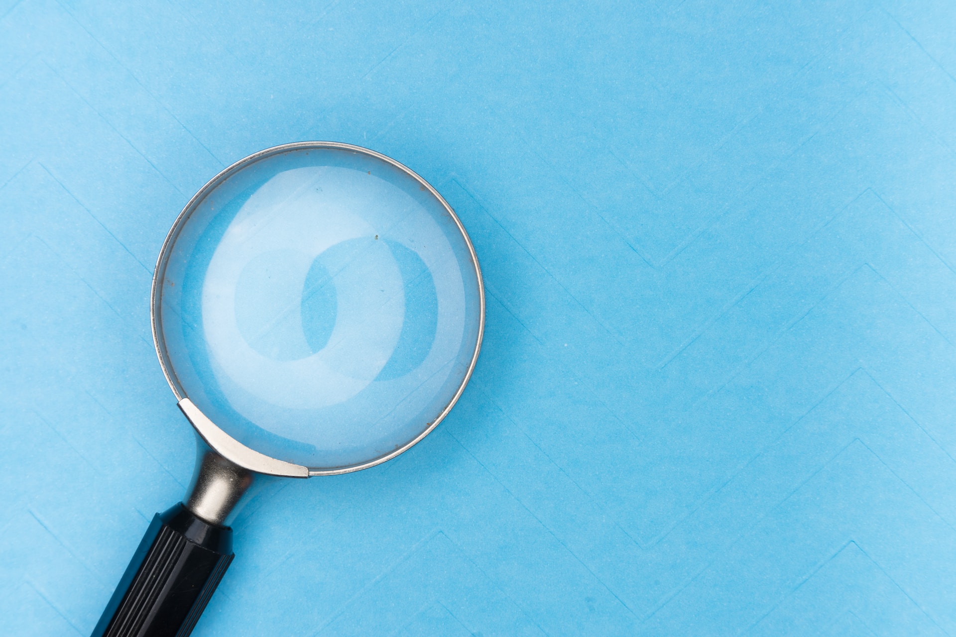 A handheld magnifying glass resting on a blue background