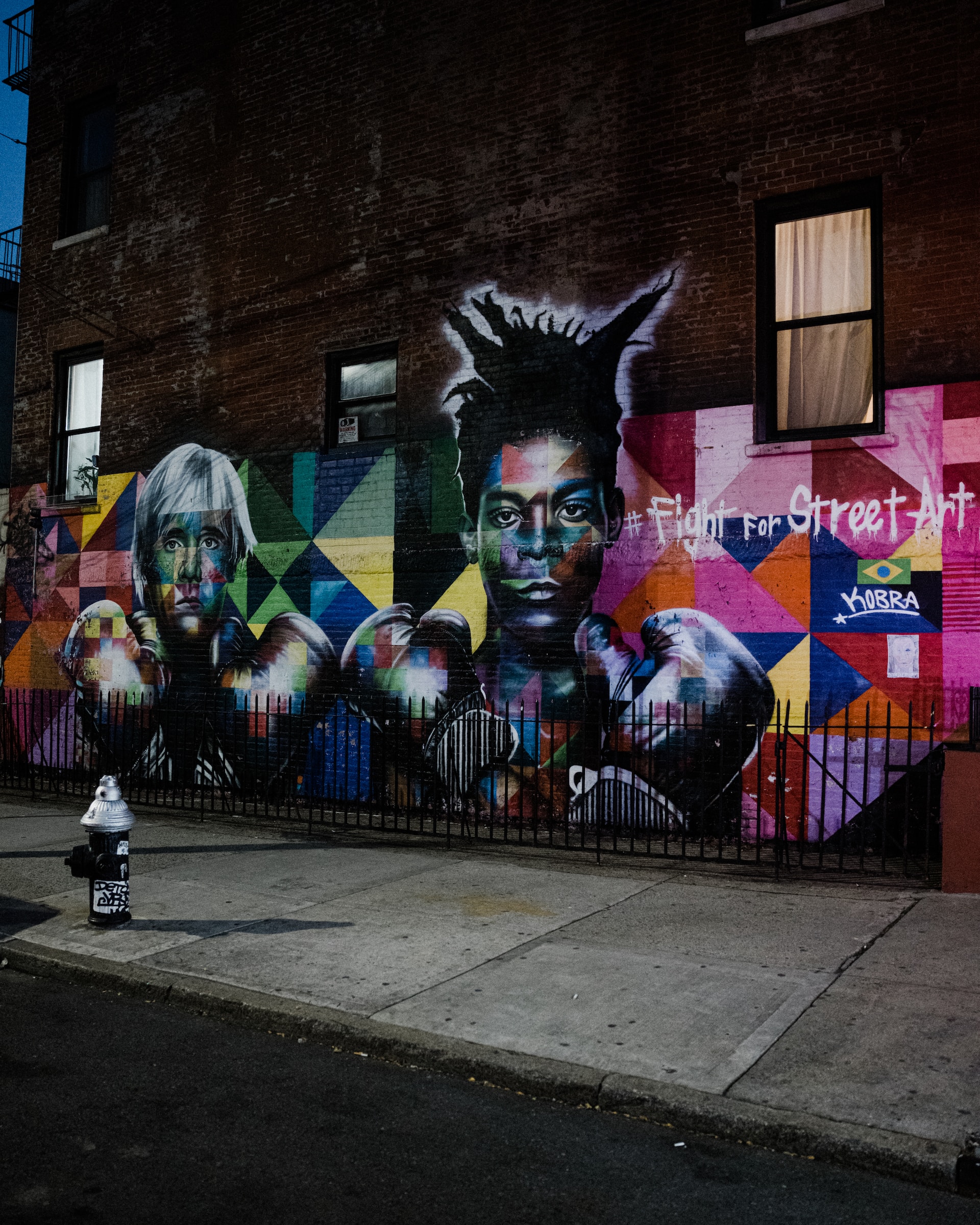grafitti mural on a brick wall featuring andy warhol and basquiat wearing boxing gloves